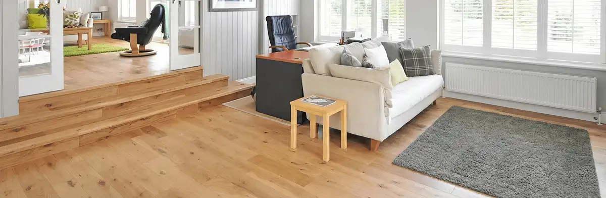 A modern living room with professionally installed laminate flooring, a beige sofa, a small side table, a gray rug, and large windows with white shutters in Myrtle Beach, SC